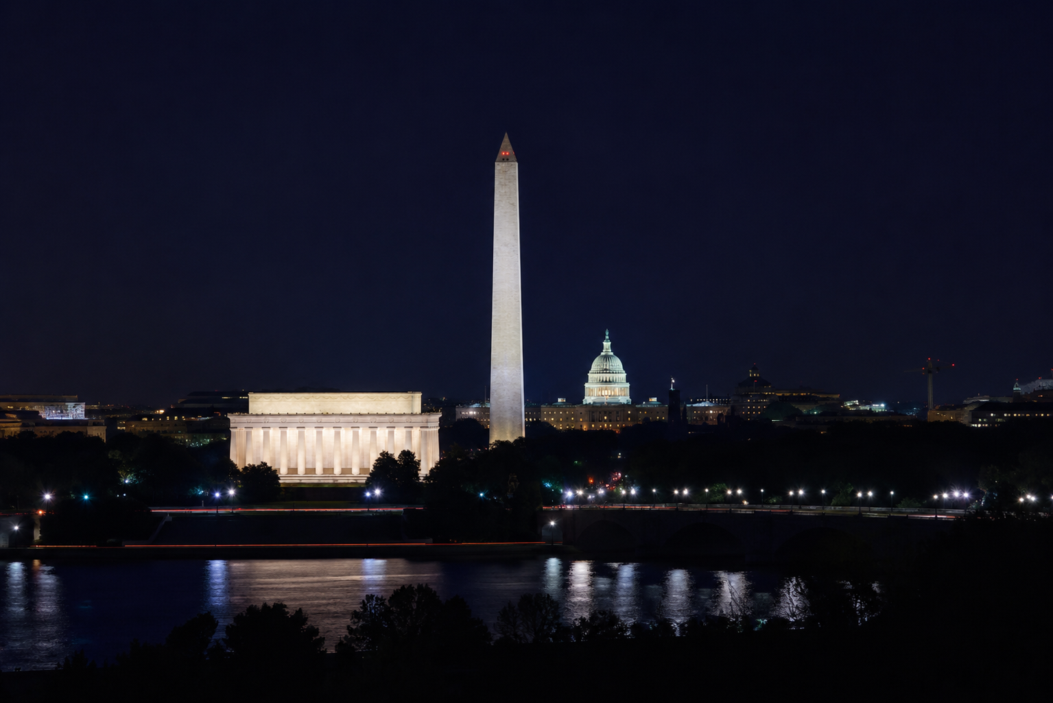 The Washington DC skyline at night with the reflecting pool in the foreground. The US Capitol, Washington Monument and Lincoln Memorial are visible.